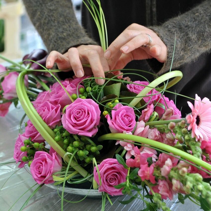 Hands arranging pink rose and greenery bouquet